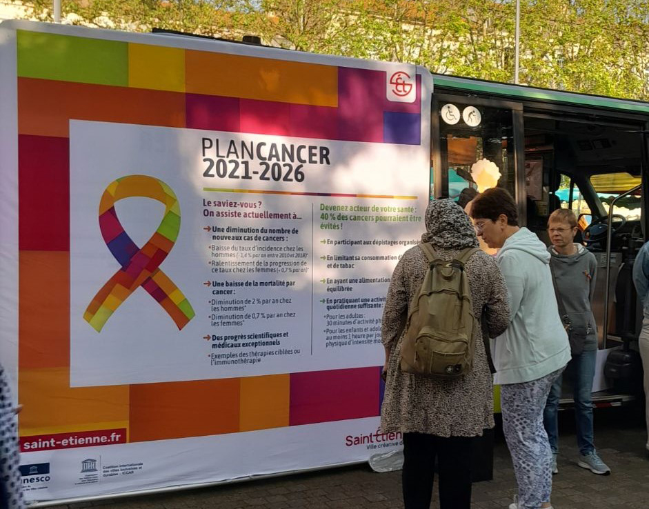 un groupe de femmes devant un panneau explicatif sur le plan cancer 2021-2026