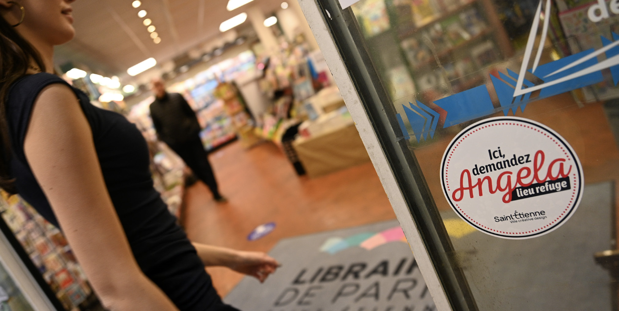 une femme qui rentre dans un magazin avec une pastille "Ici, demandez Angela" sur la porte