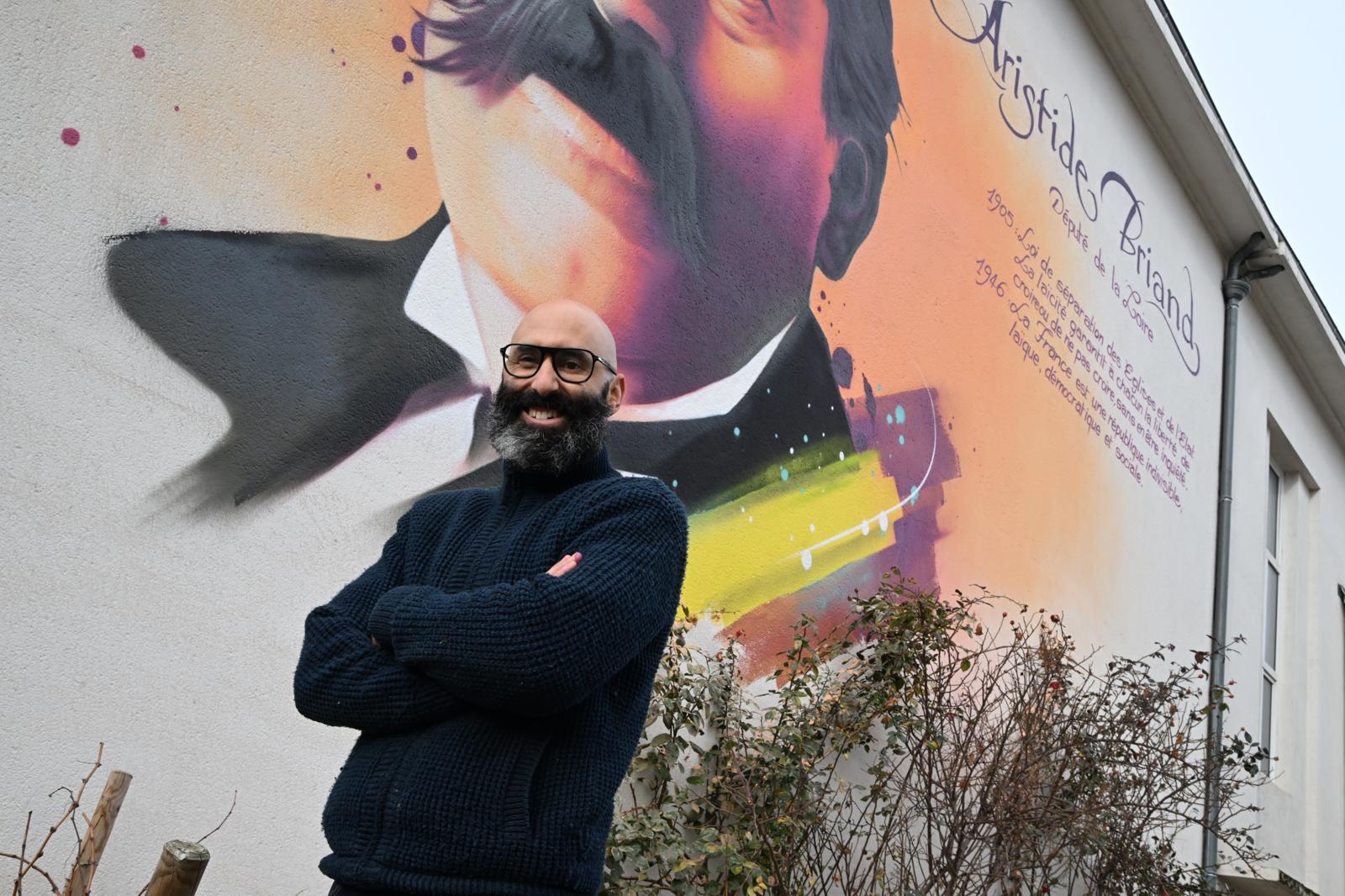 un homme souriant devant une fresque murale