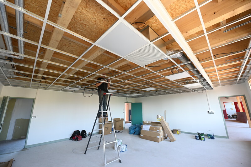 une grande pièce en chantier, un ouvrier qui travaille au niveau du plafond