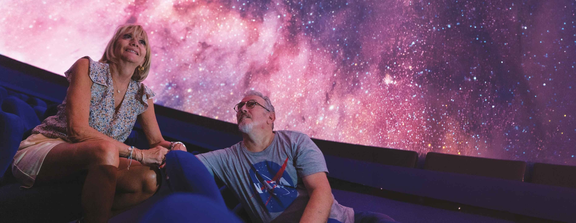 un homme et une femme regardent l'univers sous la coupole d'un planétarium