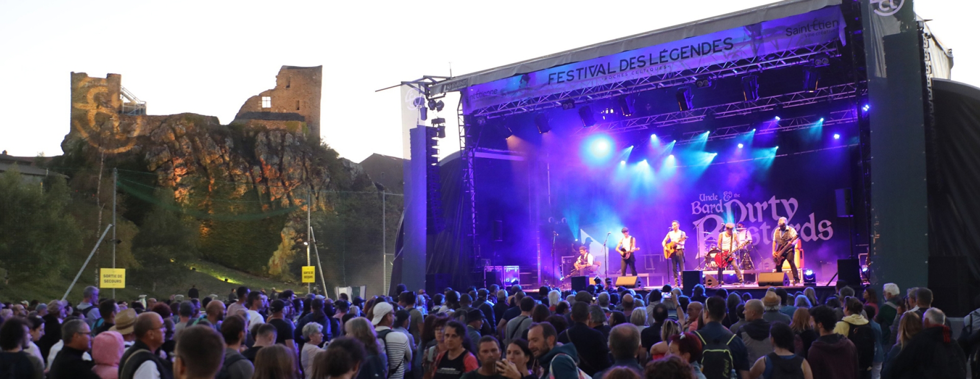 concert sur scène, devant une foule, à droite un château médiéval