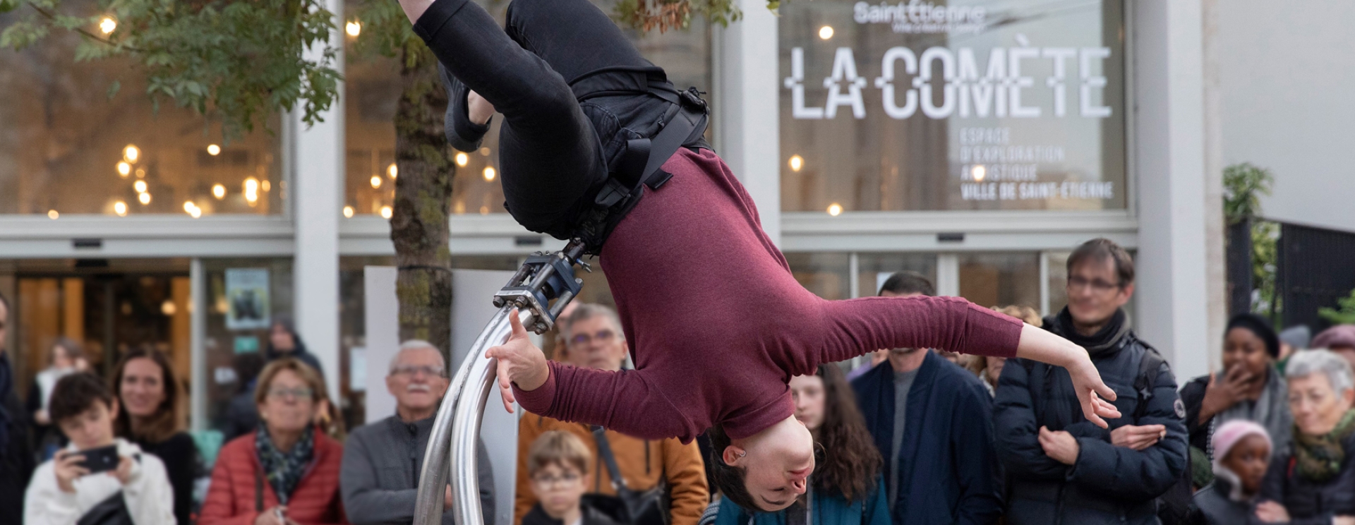 Une femme qui fait une acrobatie devant du public et le bâtiment "La Comète"