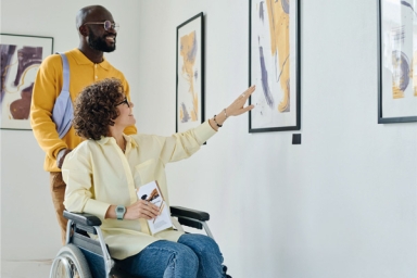 Deux personnes dont une en fauteuil roulant qui observent des tableaux
