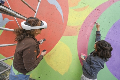 une femme avec un casque réalité virtuelle et une autre qui peint une fresque