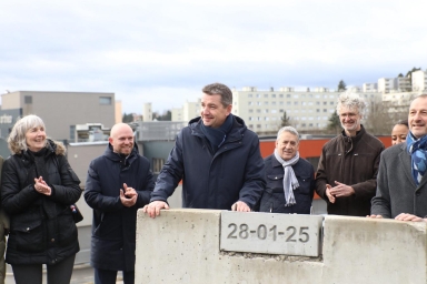 Le maire de Saint-Étienne Gaël Perdriau, entouré de plusieurs personnes souriantes et applaudissant, pose la main sur une pierre symbolique avec la date "28-01-25".