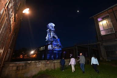 un groupe devant un chevalement de mine éclairé de nuit