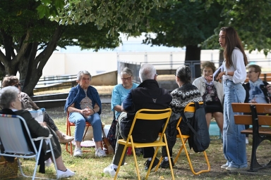 Des personnes discutant sur des chaises, et une jeune animatrice debout