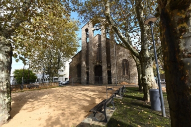 place avec des arbres, un sol ensablé, un banc et une église