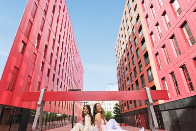 deux jeunes femmes sur un grand banc rouge avec des immeubles rouges en arrière-plan - Agrandir l'image 1 sur 4, fenêtre modale