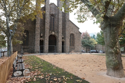 place avec des arbres, un sol ensablé, un banc et une église - Agrandir l'image 2 sur 2, fenêtre modale