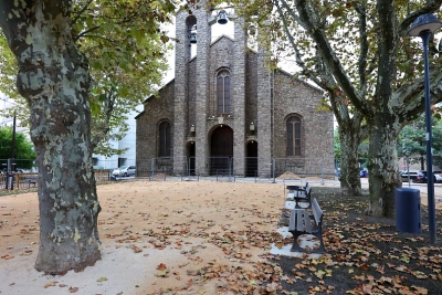 place avec des arbres, un sol ensablé, un banc et une église - Agrandir l'image 1 sur 2, fenêtre modale
