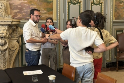Un homme interrogé au micro par un groupe de personnes - Agrandir l'image, fenêtre modale