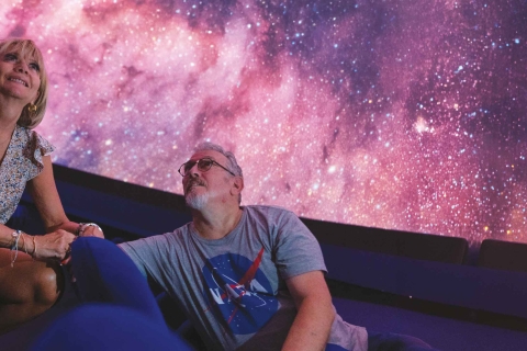 un homme et une femme regardent l'univers sous la coupole d'un planétarium