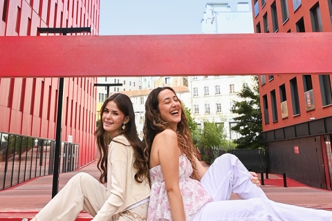 deux jeunes femmes sur un grand banc rouge avec des immeubles rouges en arrière-plan