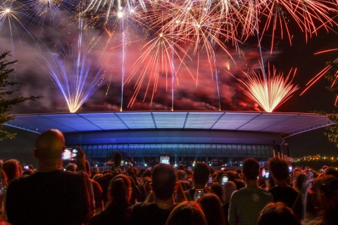 une foule devant un bâtiment surplombée d'un feu d'artifice