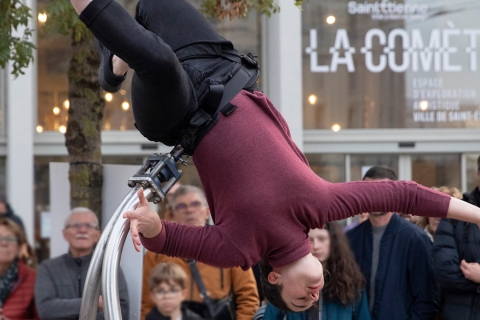 Une femme qui fait une acrobatie devant du public et le bâtiment "La Comète"