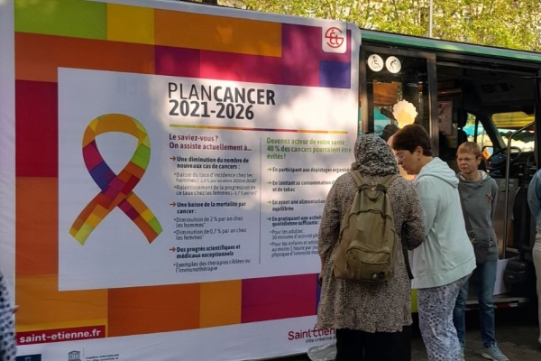 un groupe de femmes devant un panneau explicatif sur le plan cancer 2021-2026